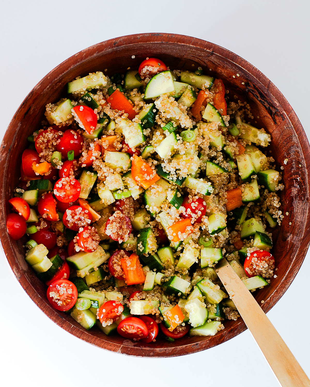 Quinoa salad with cucumber, cherry tomatoes, bell pepper and green onion tossed together in a wooden bowl