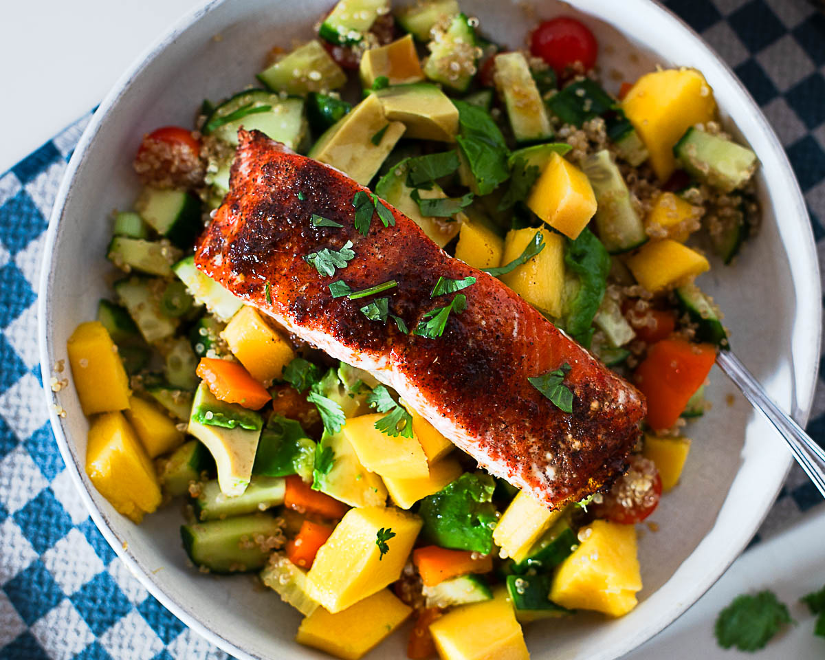Hot honey salmon quinoa bowl with a fork, showing the layers of quinoa, mango, avocado and salmon