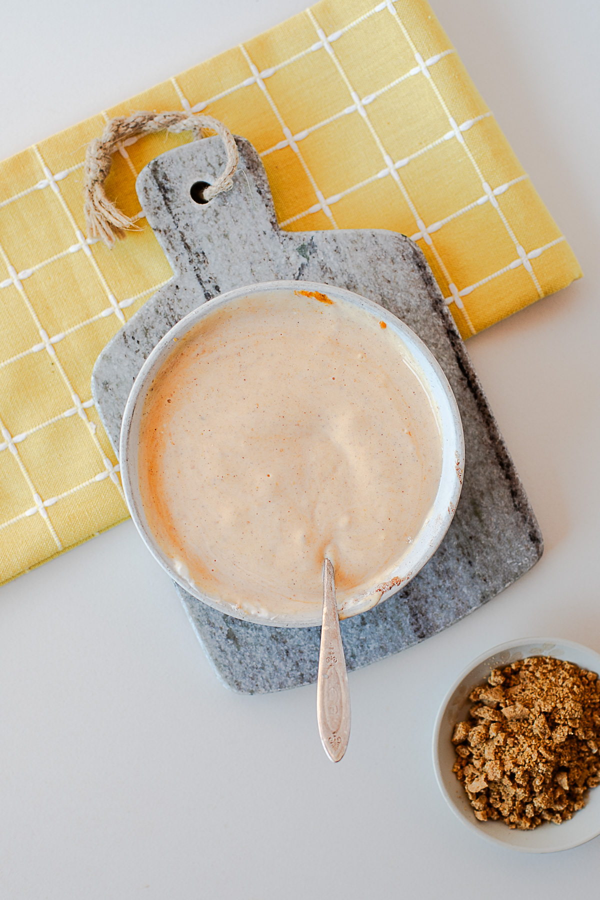 Pumpkin pie yogurt stirred together in a bowl with a spoon, with granola on the side