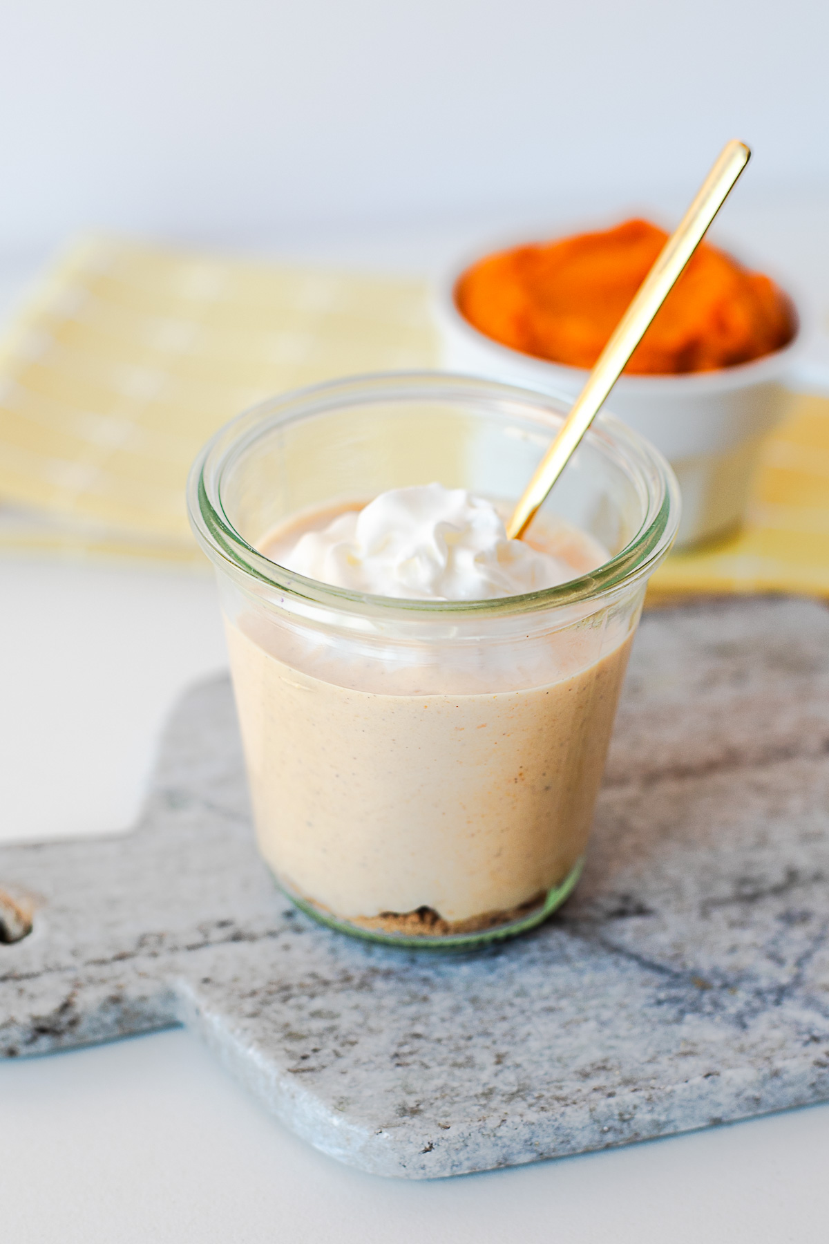 Pumpkin pie yogurt bowl with a gold spoon, whipped cream and a bowl of pumpkin puree behind it