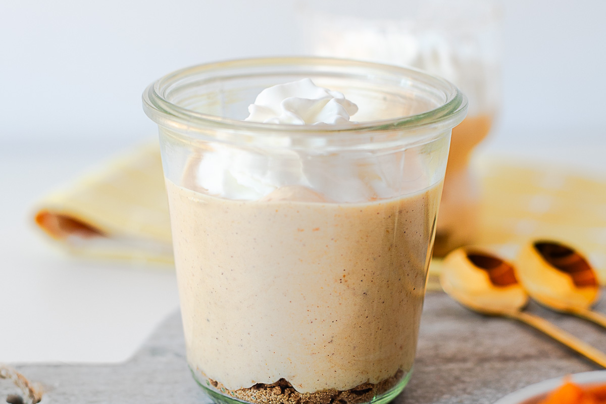 Pumpkin pie yogurt in a glass jar with whipped cream, a cookie crust and gold spoons