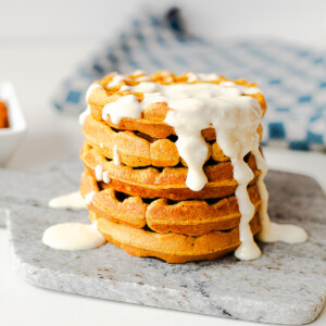 Stack of pumpkin protein waffles topped with a creamy honey cottage cheese drizzle