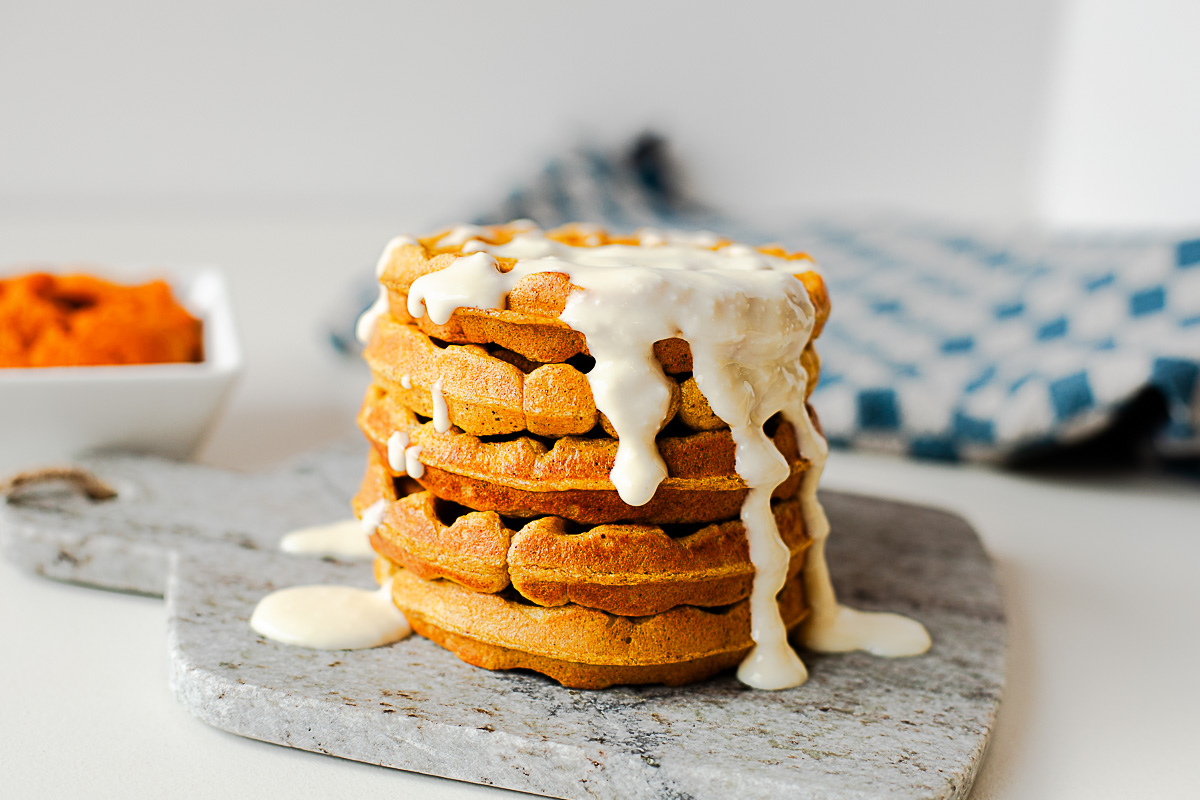 Stack of pumpkin protein waffles with honey cottage cheese drizzle and a blue checkered towel