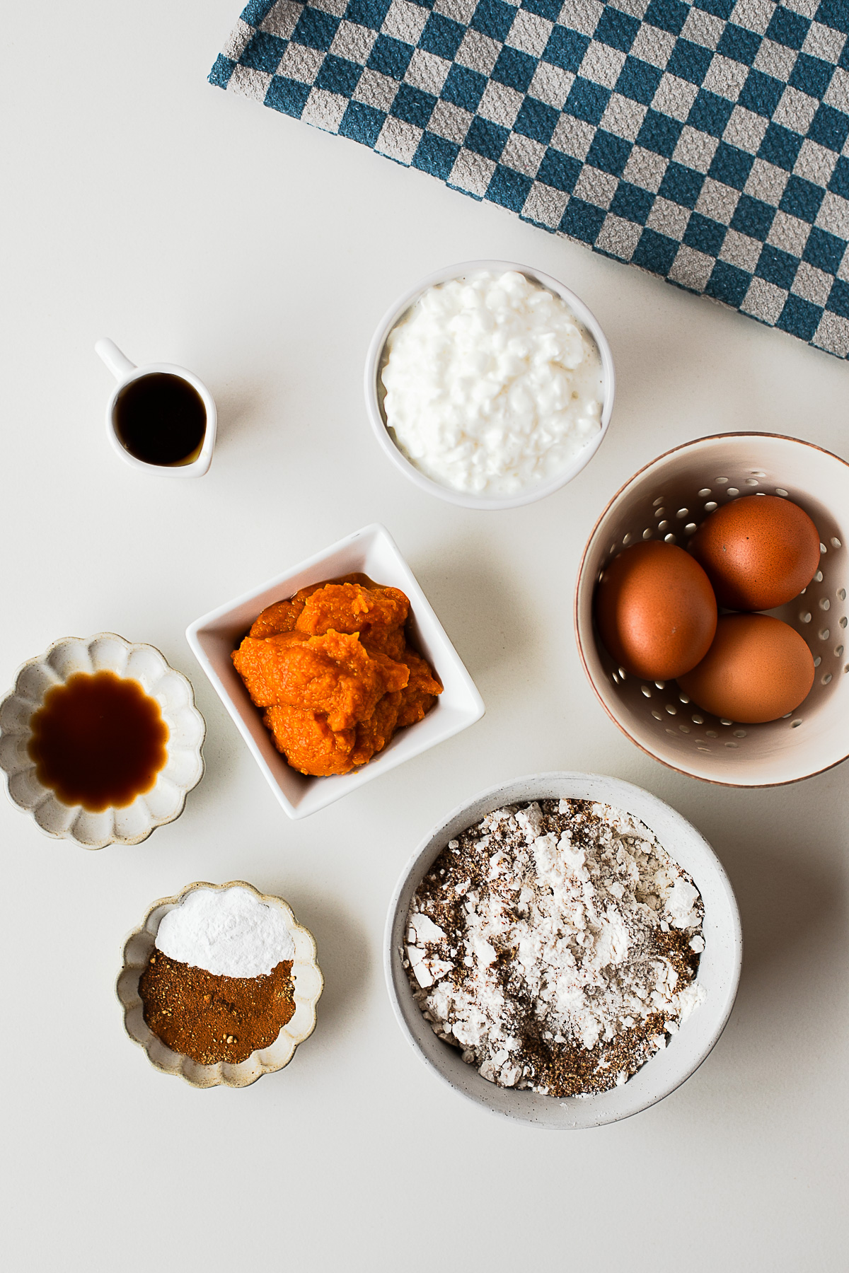 Ingredients for pumpkin protein waffles, including pumpkin puree, cottage cheese, eggs, maple syrup, vanilla, flour, flaxmeal and spices