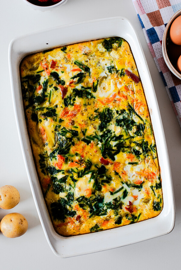 Baked smoked salmon and potato breakfast casserole in a white dish, golden and set with spinach and salmon visible throughout.